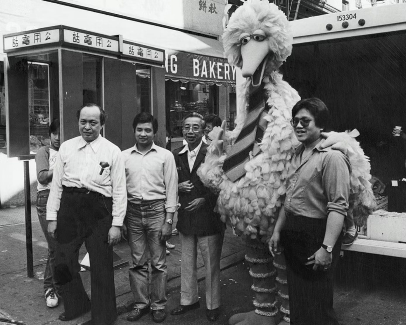 Big Bird posing with Peter Lee (left of Big Bird) and his son Paul Lee (right of Big Bird), owners of the shop Quong Yuen Shing at 32 Mott Street, which was featured in the children’s television special Big Bird in China, and two unknown men, June 10, 1982. Photograph taken by Emile Bocian, Museum of Chinese in America (MOCA) Collection.