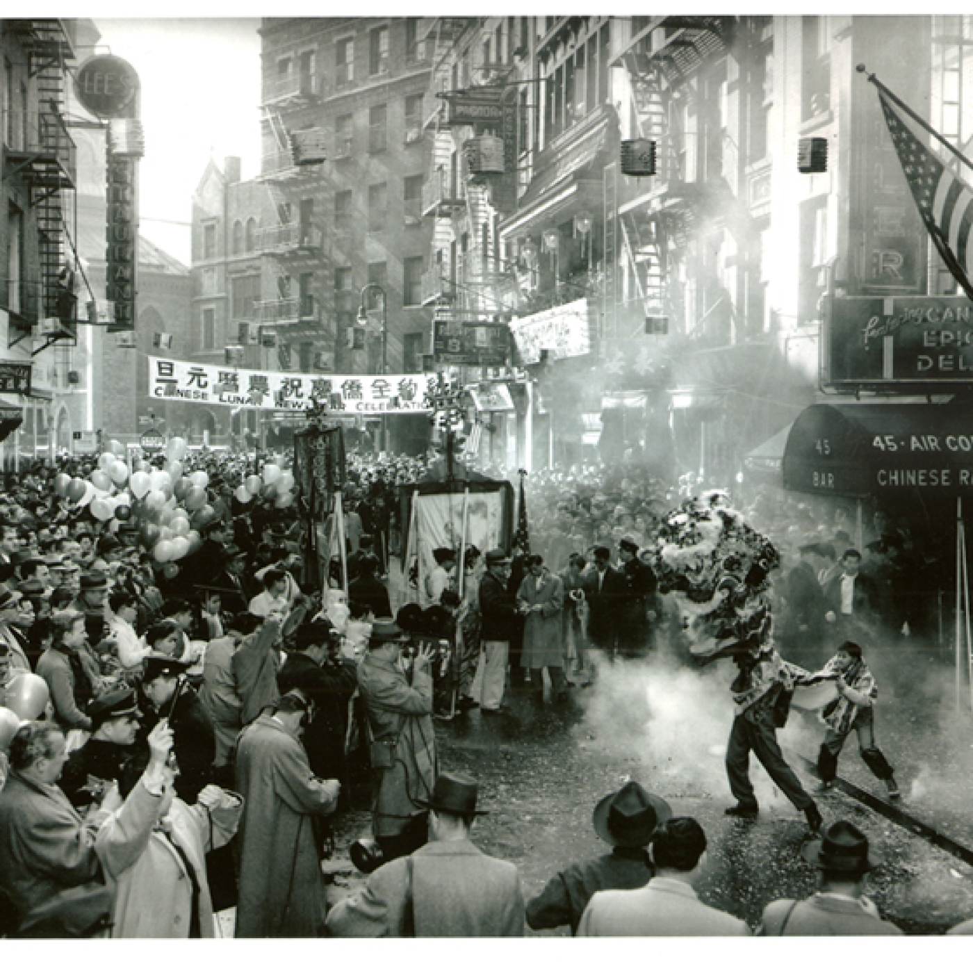 2015.043.032 Crowds flood the streets to see a lion dance outside the Chinese Rathskeller Restaurant on 45 Mott Street during a Chinese Lunar New Year Celebration. Other shops on the street include Pagoda Restaurant, Lee's Restaurant, Typond & Lee, Po On Co. It is a grand celebration with balloons, confetti, firecrackers, and a parade with dancers and portable shrines, undated. Courtesy of Eric Y. Ng, Museum of Chinese in America (MOCA) Collection. 2015.043.032 在纽约华人农历新年庆祝活动期间，人群涌入街道，观看位于勿街 45 号的中国 Rathskeller 餐厅外的舞狮。街上的其他商店包括 Pagoda 餐厅、Lee's 餐厅、Typond & Lee、Po On Co.。这是一个盛大的庆祝活动，有气球、五彩纸屑、鞭炮，还有舞者和便携式神龛的游行，日期不详。由伍锐贤提供，美国华人博物馆 (MOCA) 馆藏。