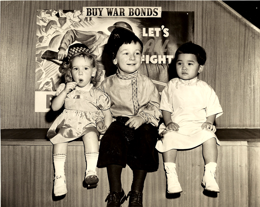 2004.029.007 Three children—one Scottish, one Russian, and one Chinese—were chosen by artist Margery Ryerson to be models for paintings to be used by the Ninth Federal Savings and Loan Association at 1457 Broadway, New York, NY to boost the sale of war bonds. The children are, from left to right: Susan Murray, of Stillwell Avenue, Brooklyn; Andriusha Branitzka, of 57th Street, Manhattan; and Virginia Chin (née Lee), of 73 Mulberry Street, Manhattan. Photograph taken by Larry Gordon. Courtesy of Virginia S. Chin, Museum of Chinese in America (MOCA) Collection.