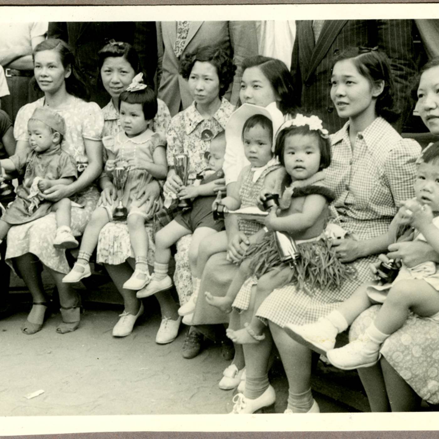 2012.002.002 A group photograph of the participants in the New York City Chinatown baby contest held on June 17, 1939 in Columbus park. Second from the right are mother and daughter Vivian Dai and Meling Dai (18 months). Third from the right are Meme Chen with her daughter Jaqueline Young (2 years). First from the left are May Moy with Patricia Moy (2 years). Third from left are Grace Lee Mok and her daughter Jade Mok, who won the prize for healthiest girl. Pictured at far right is Rose Lee Liu, wife of Dr. Arthur Liu, with her son Allan Liu. The Commissioner of Health and policemen, standing behind them, were the guests of honor. Courtesy of Meiling Dai, Museum of Chinese in America (MOCA) Collection. 1939年6月17日在哥伦布公园举行的纽约市唐人街婴儿比赛参赛者合影。右二是Vivian Dai 和Meling Dai（18个月）和她们的妈妈。右三是 Chen女士 和她的女儿 Jaqueline Young（2 岁）。左起第一是 May Moy 和 Patricia Moy（2 岁）。左三是Grace Lee Mok和她的女儿Jade Mok，她获得了最健康女孩奖。最右边的照片是 Arthur Liu 博士的妻子 Rose Lee Liu 和她的儿子 Allan Liu。站在他们身后的卫生署署长和警察是贵宾。由Meiling Dai捐赠，美国华人博物馆（MOCA）馆藏。