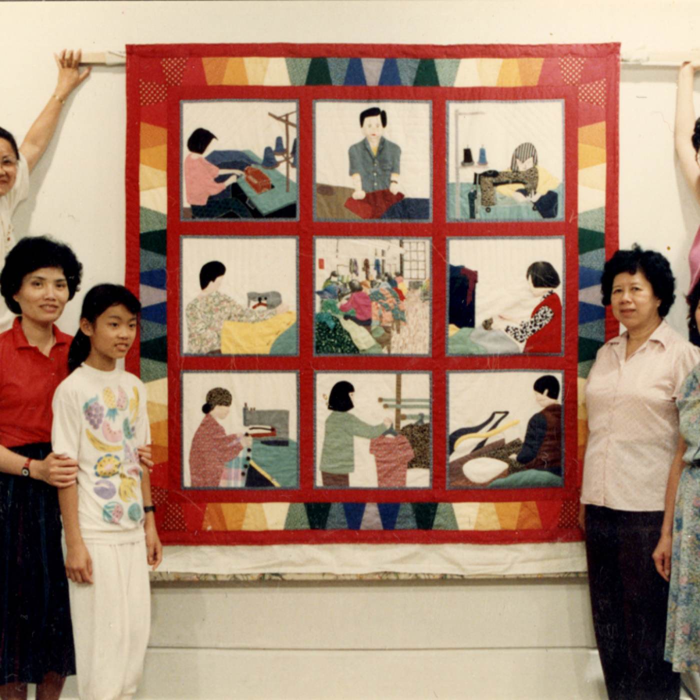 Quilt maker Debbie S. Lee (top right) collaboratively created the Garment Workers Quilt with Yan Chai Mak, Cecilia Lo, Ng Mui Leung, Sheung Ngor Leung, So Fong Lee Ng, Sun Ng, and Heng Yu Yan, all garment workers in New York Chinatown. Here they are posed on either side of a display of their quilt at MOCA’s 1989 exhibit, “Both Sides of the Cloth.” Museum of Chinese in America (MOCA) Collection.
