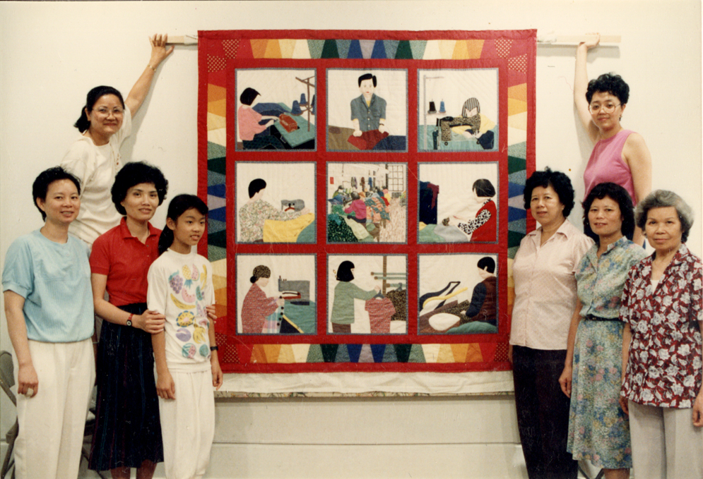 Quilt maker Debbie S. Lee (top right) collaboratively created the Garment Workers Quilt with Yan Chai Mak, Cecilia Lo, Ng Mui Leung, Sheung Ngor Leung, So Fong Lee Ng, Sun Ng, and Heng Yu Yan, all garment workers in New York Chinatown. Here they are posed on either side of a display of their quilt at MOCA’s 1989 exhibit, “Both Sides of the Cloth.” Museum of Chinese in America (MOCA) Collection.