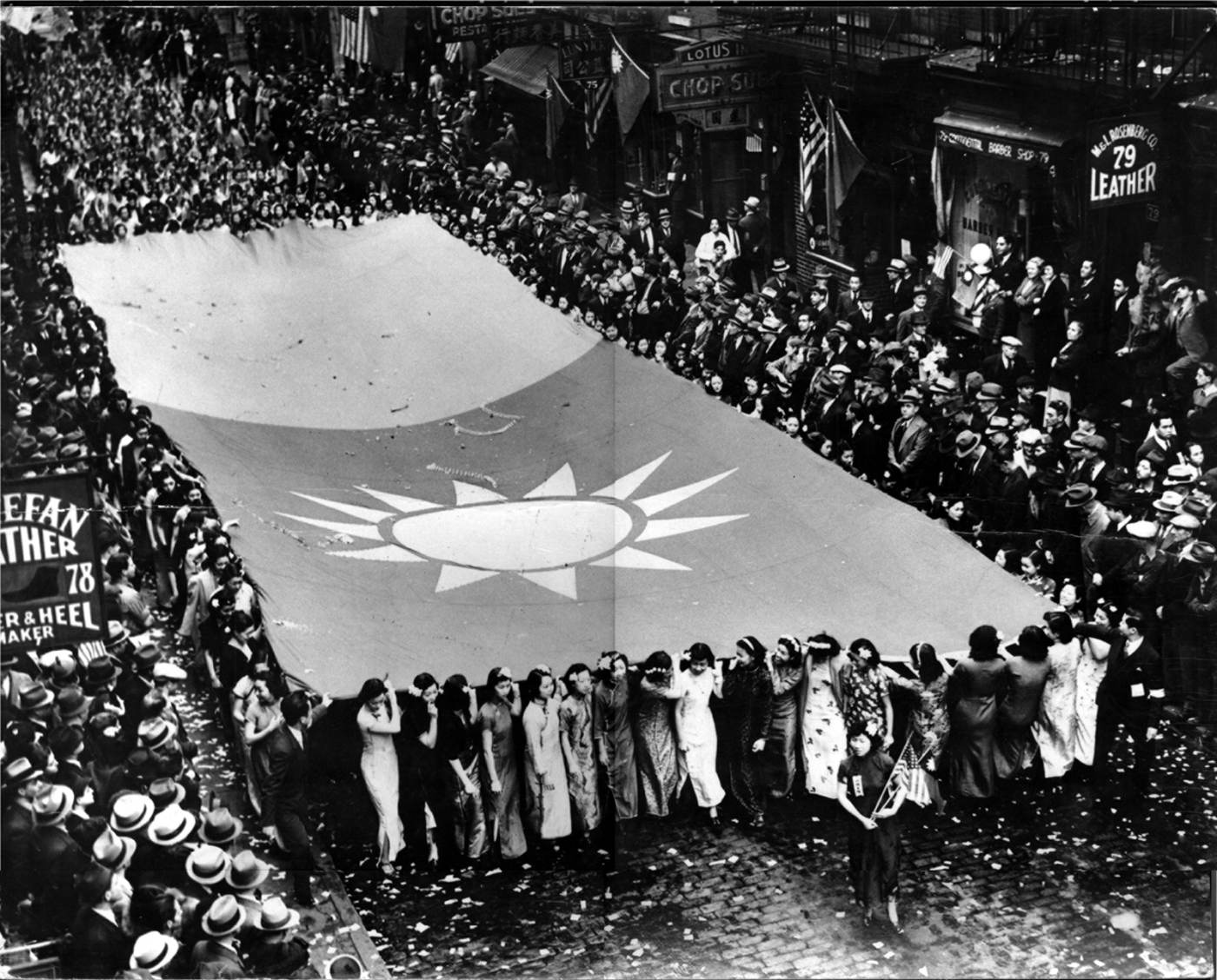 Condition pre-fire. Mounted black and white photograph of marchers carrying a giant Chinese national flag in a 1938 show of unity parade supporting China's war of defense against Japan. Courtesy of Warren Chan, Museum of Chinese in America (MOCA) Collection. 