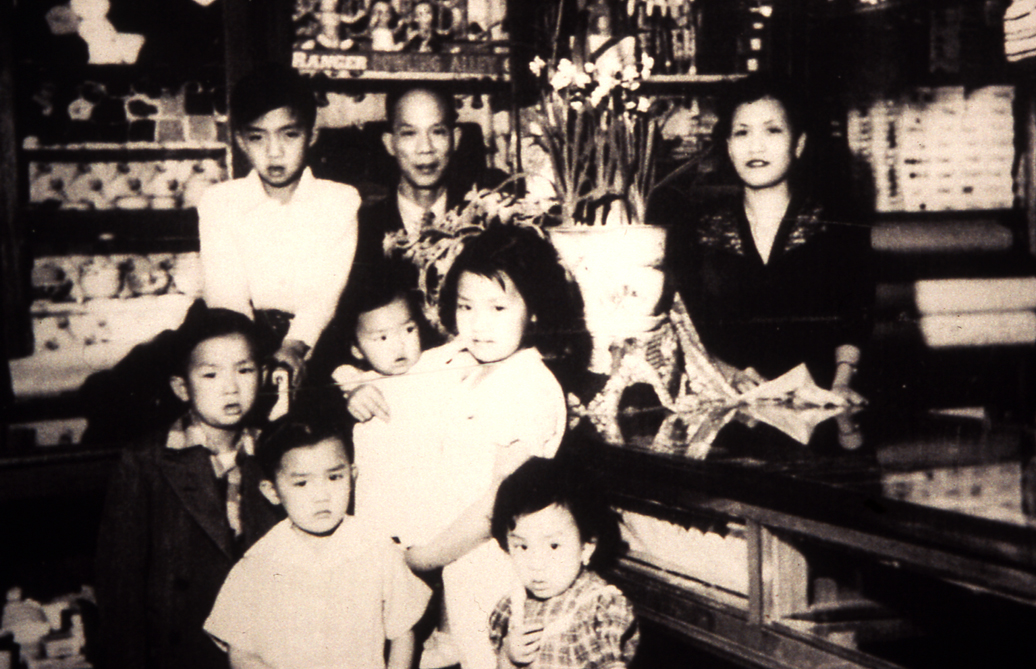 2011.031.003 Don Rodolfo Lau and family in Almacén El Bien Mutuo, 5a. avenida, Guatemala City, early 1950s. First row, left to right: Alberto, Esperanza. Second row, left to right: Armando, Amelia, Gloria. Third row, left to right: Adolfo, don Rodolfo, doña Graciela Chang de Lau. Courtesy of Amelia Lau Carling, Museum of Chinese in America (MOCA) Collection.