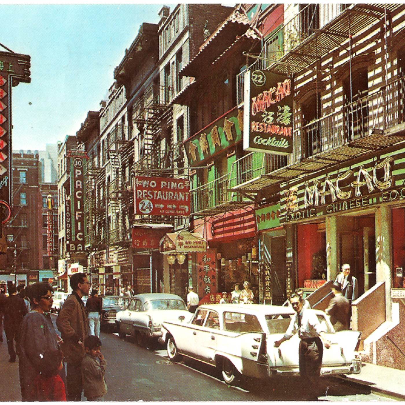2015.043.336-a This postcard shows a view of Pell Street in 1968 with an assortment of restaurants and places including the Chinese Conservative Baptist Church, Macao Restaurant on 22 Pell, Shanghai Restaurant on 23 Pell, Wo Ping Restaurant on 24 Pell, and Pacific Restaurant on 30 Pell. There are people and now antique automobiles on the streets. Courtesy of Eric Y. Ng, Museum of Chinese in America (MOCA) Collection.
