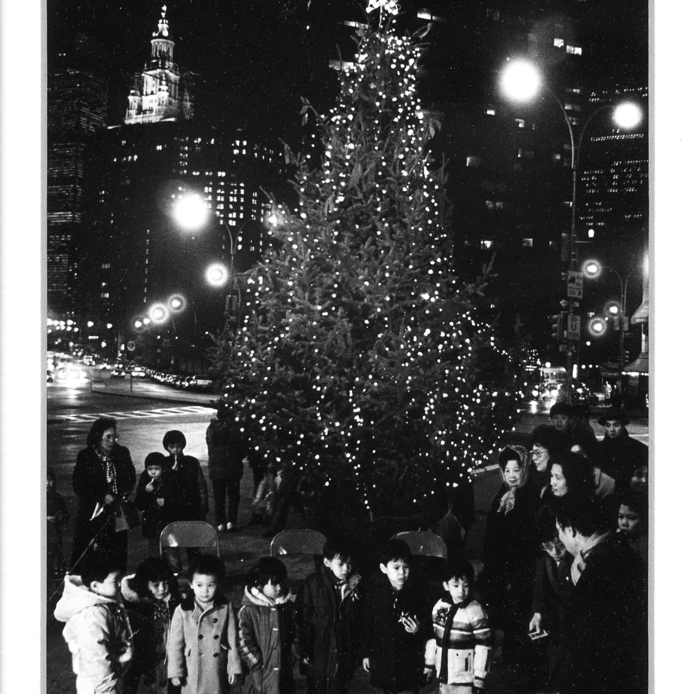 2011.046.008 This photograph, taken by Poon Waterfield, shows families at the celebration of the first Christmas tree ever in Chatham Square, December 1986. Courtesy of Poon Waterfield, Museum of Chinese in America (MOCA) Faces of Chinatown Collection.