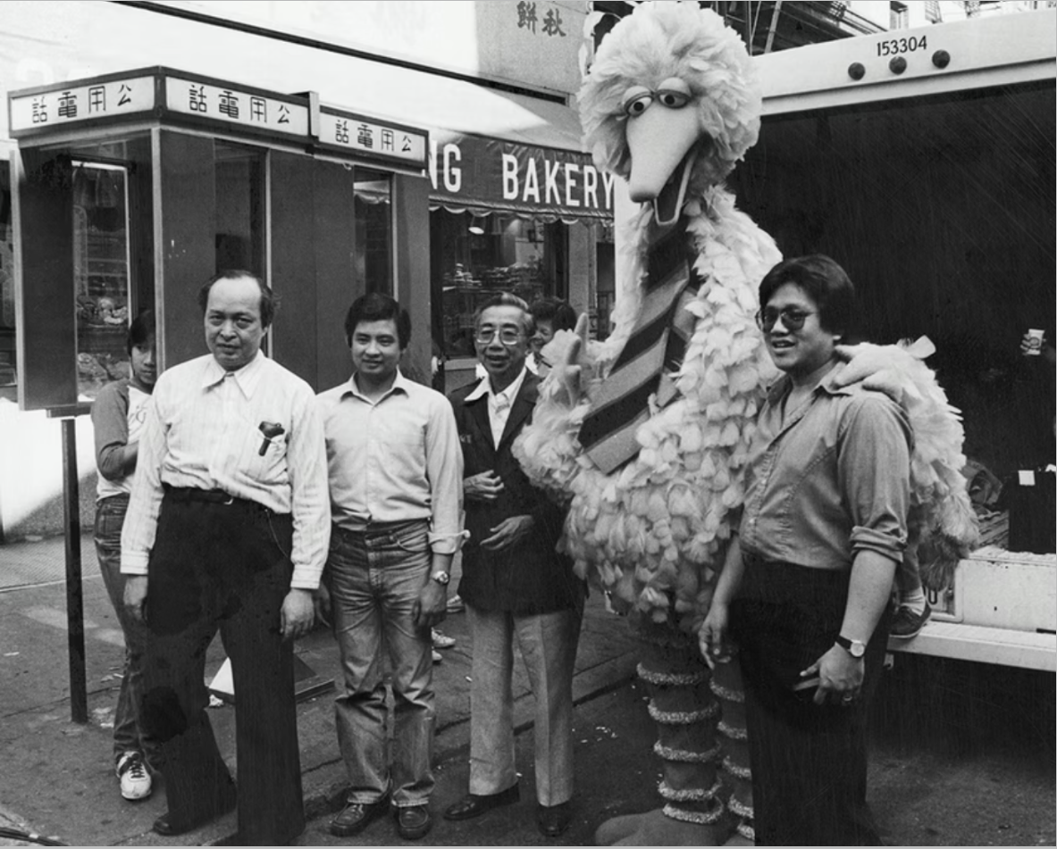 Big Bird posing with Peter Lee (left of Big Bird) and his son Paul Lee (right of Big Bird), owners of the shop Quong Yuen Shing at 32 Mott Street, which was featured in the children’s television special Big Bird in China, and two unknown men, June 10, 1982. Photograph taken by Emile Bocian, Museum of Chinese in America (MOCA) Collection.