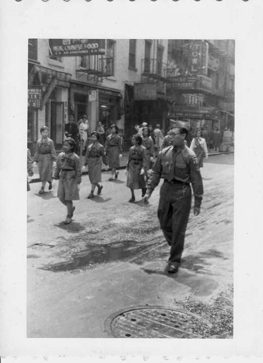 2006.004.447 Man wearing a scouting uniform leading a group of Girl Scouts down a street in New York’s Chinatown. The girls are wearing 1940s era Girl Scout uniforms. Courtesy of Marcela Dear, Museum of Chinese in America (MOCA) Collection. 