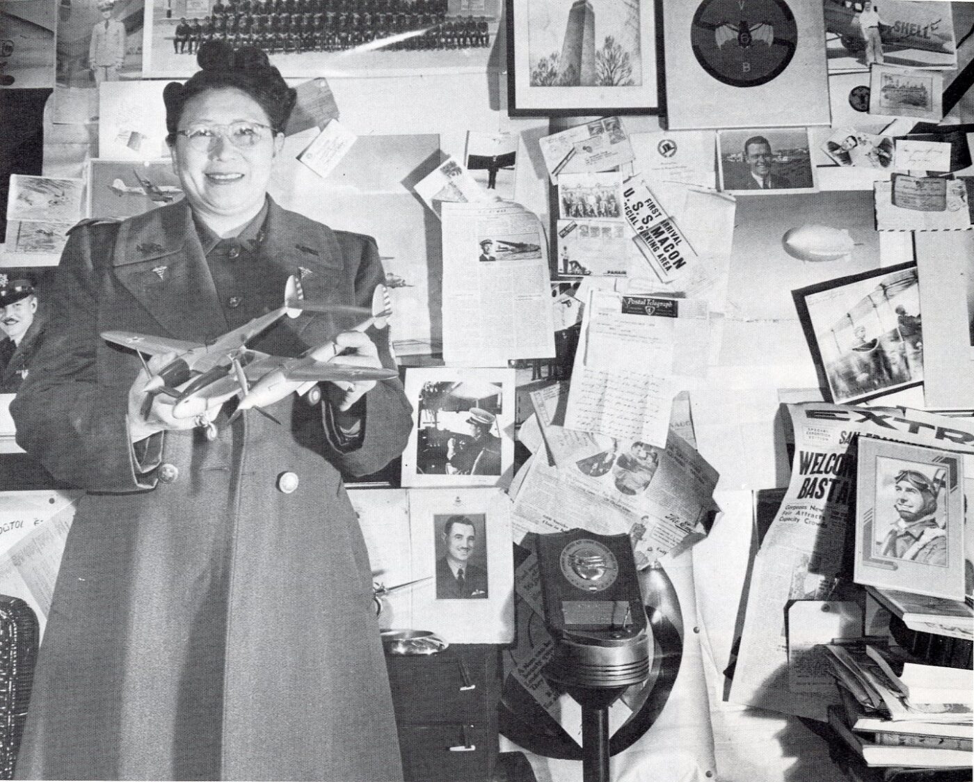 张玛珠（Margaret Jesse Chung）医生手持一架洛克希德P-38“闪电”式战斗机模型，背景是她协助招募加入“飞虎队”的几位“养子”的照片。图片转载自谭碧芳（Judy Yung）所著《美国华人女性：图文史》（*Chinese Women of America: A Pictorial History*，华盛顿大学出版社，1986年），美国华人博物馆（MOCA）图书馆馆藏。
